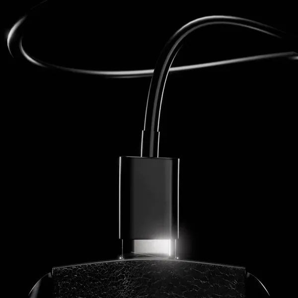 Svart USB-C ladekabel koblet til Bathmate Trim 2.0 kroppstrimmer med teksturert overflate mot mørk bakgrunn.