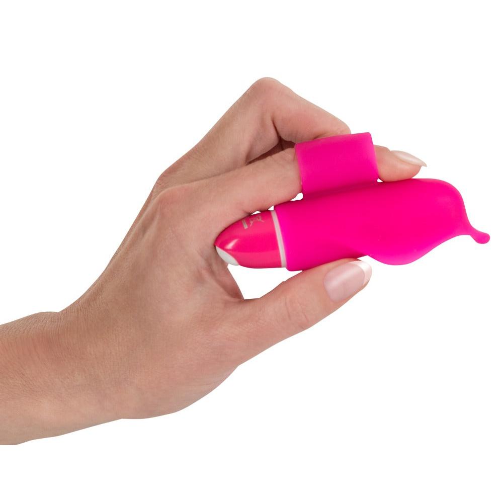 En hånd holder en liten, rosa delfinformet silikon klitorisvibrator med fingerstropp.