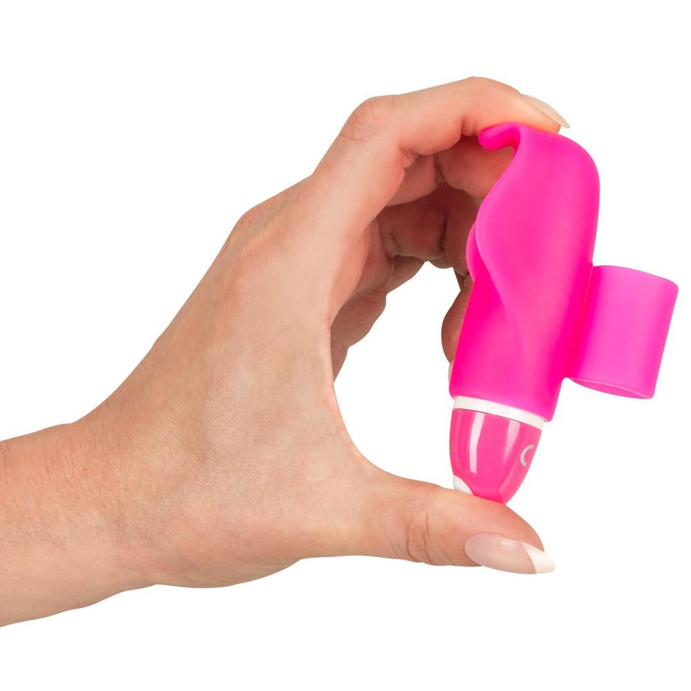 En hånd holder en liten, rosa delfinformet klitorisvibrator i silikon med hvite detaljer.