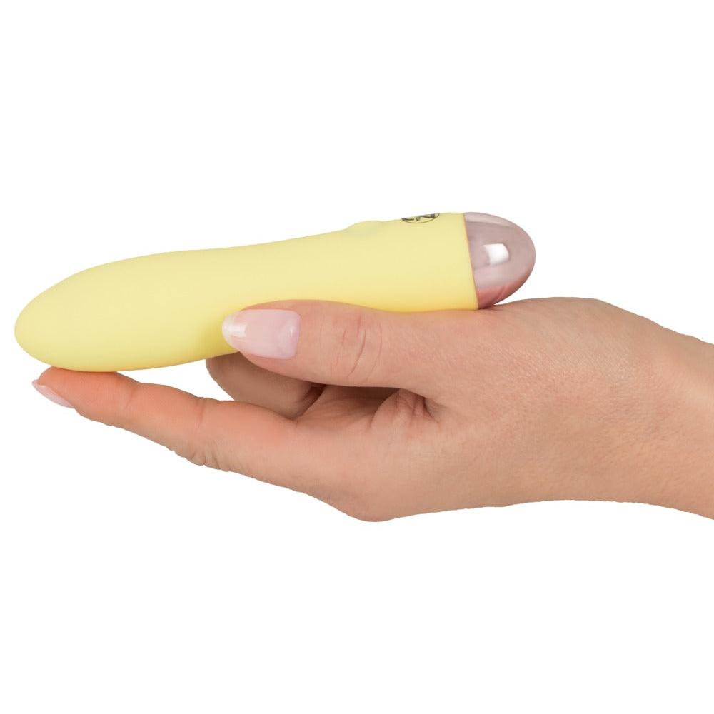En hånd holder en liten, gul silikonvibrator med en rosa, avrundet tupp.