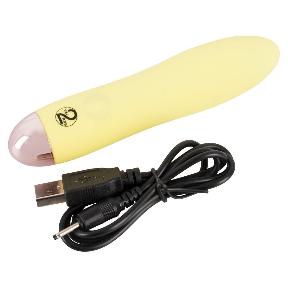 Gul, silkemyk Mini Cutie klitorisvibrator med avrundet tupp og USB-ladekabel.