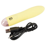 Gul, silkemyk Mini Cutie klitorisvibrator med avrundet tupp og USB-ladekabel.