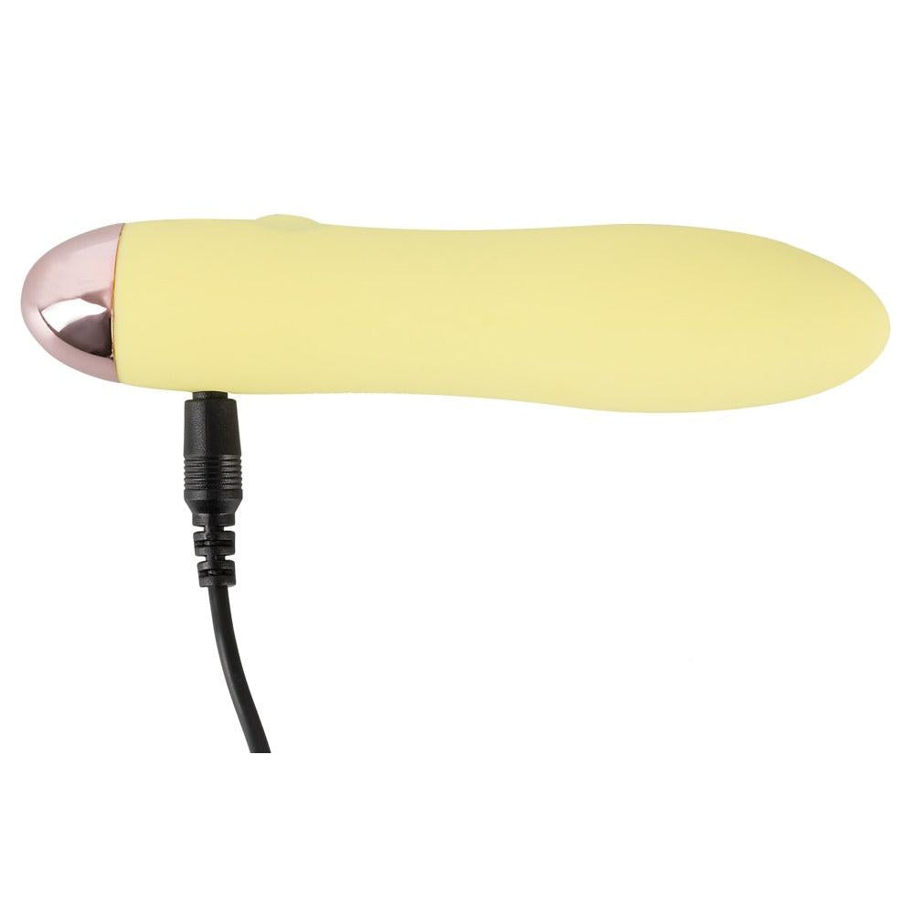 Gul Mini Cutie klitorisvibrator i silikon med rosegull tupp og svart ladekabel.