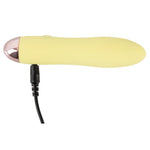 Gul Mini Cutie klitorisvibrator i silikon med rosegull tupp og svart ladekabel.