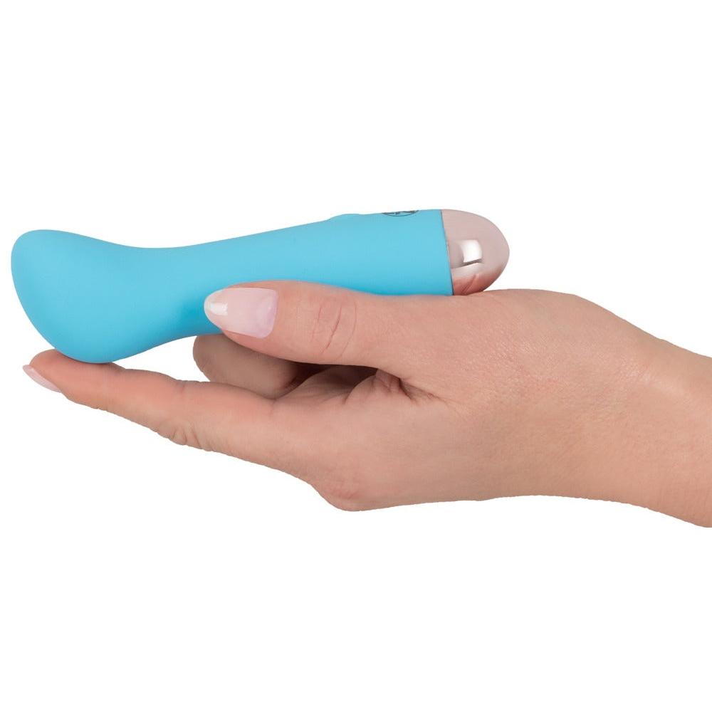 En hånd holder en liten, turkisblå klitorisstimulator med en buet tupp og metallisk base.