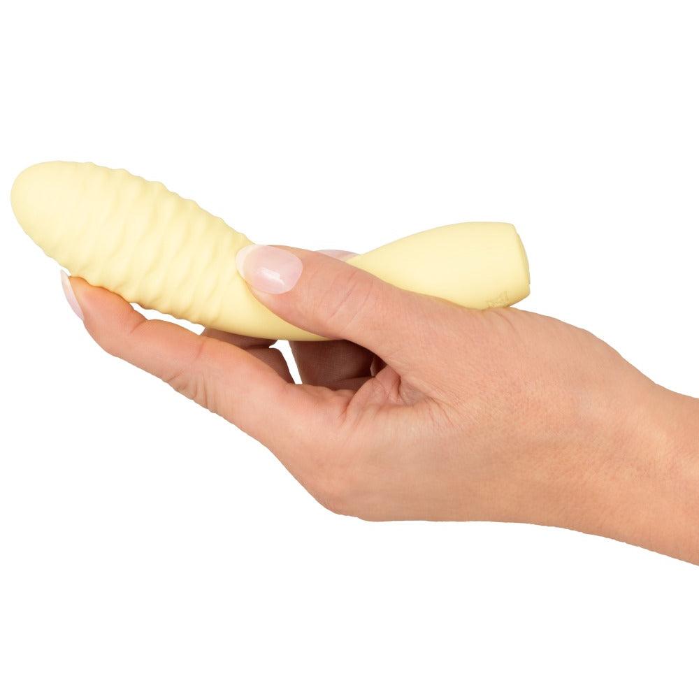 Gul, strukturert Cuties klitorisvibrator i silikon holdt i en hånd.