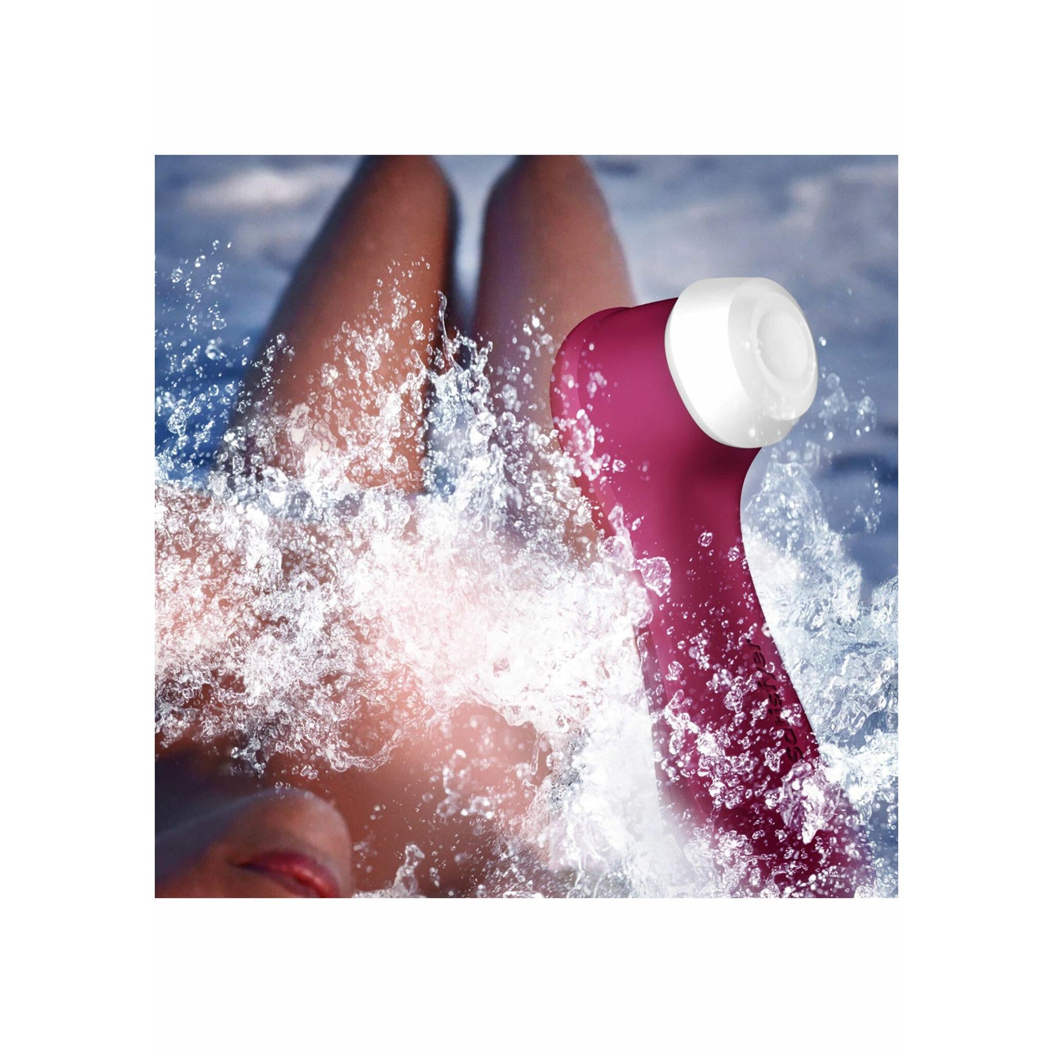 Satisfyer Pro 2 Gen 3 i mørk rosa silikon med hvit tupp, omgitt av vannsprut.