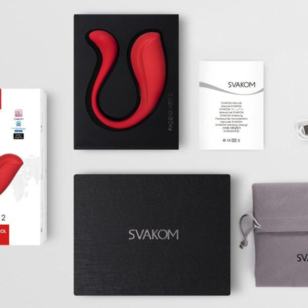 Rød, S-formet SVAKOM Phoenix Neo 2 parvibrator, eske, ladekabel, manual og oppbevaringspose.
