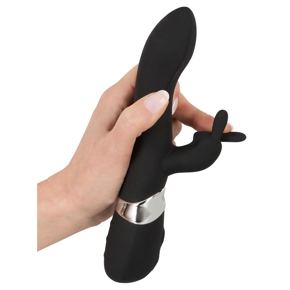 Hånd holder en svart silikon rabbitvibrator med sølvring, buet form og fleksible kaninører.