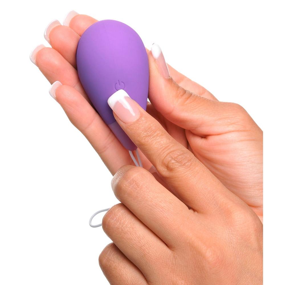 Hånd holder et lilla, silkemykt vibro-egg i kroppstrygg silikon med en av/på-knapp og uttrekksbånd.