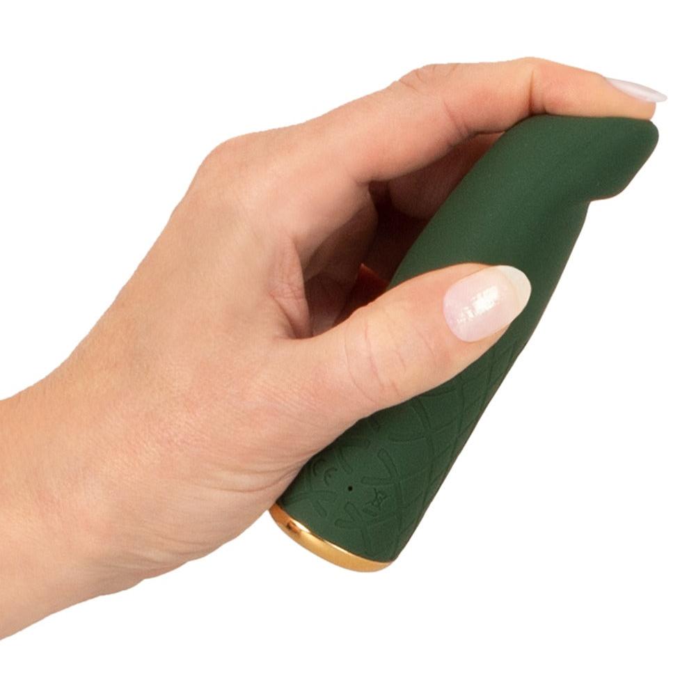 En hånd holder en mørkegrønn, silikon mini vibrator med gullbase og ruteformet tekstur.