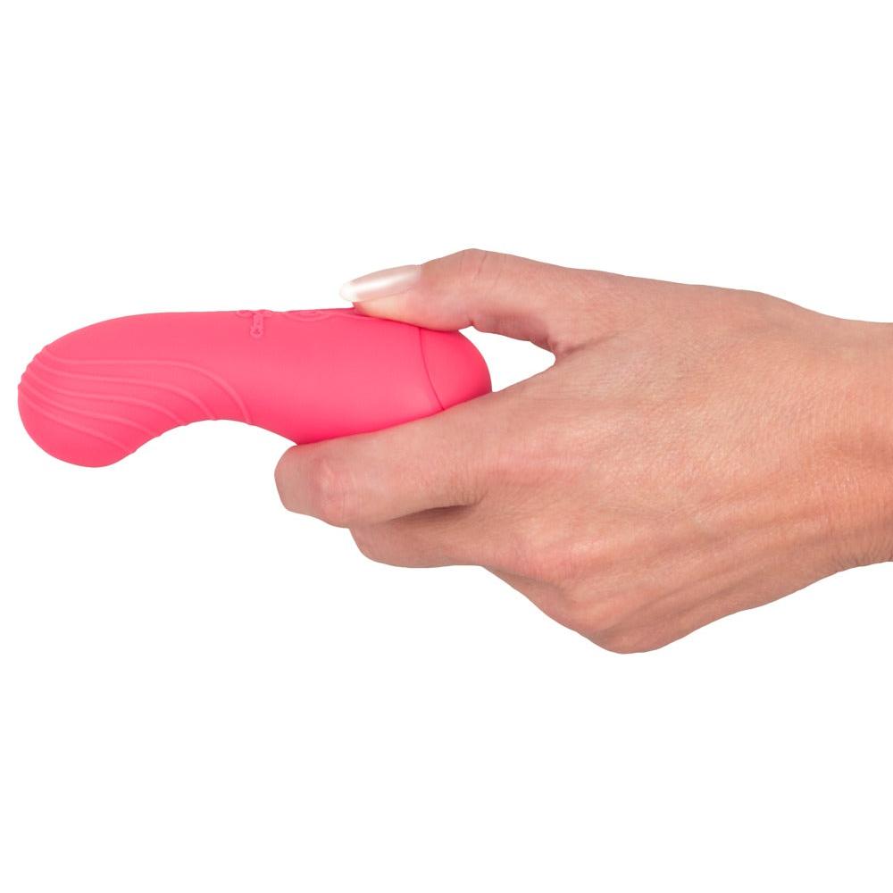Hånd holder en Corallino klitorisstimulator i silikon, lys rosa med ergonomisk form og teksturert grep.