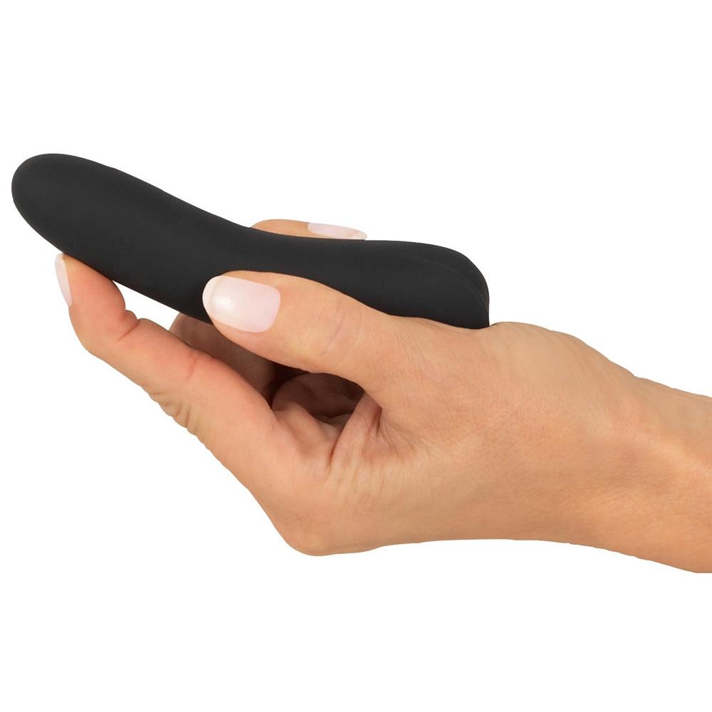 En hånd holder en liten, svart, myk Sweet Smile klitorisvibrator i silikon med buet design.