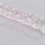 Klar glassdildo med rosa teksturerte nupper, reflektert på en hvit overflate.