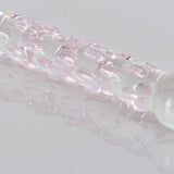 Klar glassdildo med rosa teksturerte nupper, reflektert på en hvit overflate.