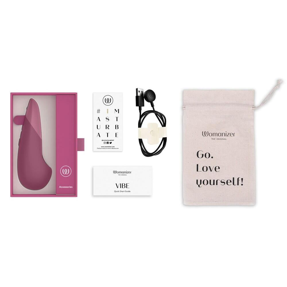 Womanizer VIBE klitorisstimulator i mørk rosa silikon, med ladeledning, instruksjoner og tøypose.