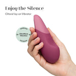 Mørk rosa Womanizer VIBE klitorisstimulator i silikon, holdt i en hånd.