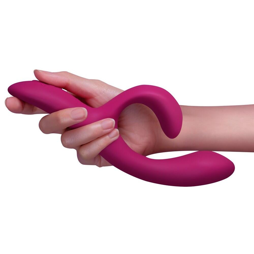Hånd holder en fleksibel, fuchsia We-Vibe Nova 2 rabbitvibrator i silkemyk silikon.