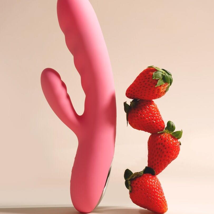 Rosa silikon rabbitvibrator med støtfunksjon, ved siden av en stabel friske jordbær.