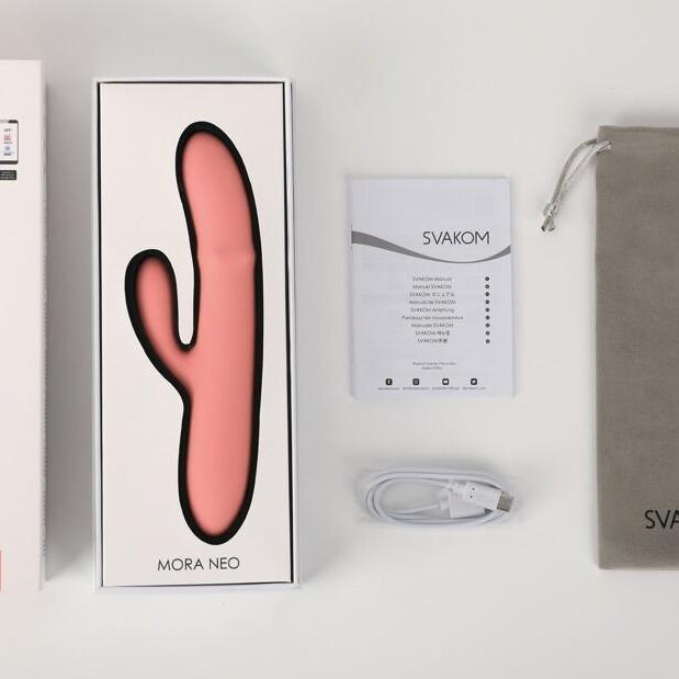 Mora Neo rabbitvibrator i rosa silikon, med emballasje, manual, ladekabel og grå oppbevaringspose.