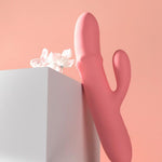 Rosa SVAKOM Mora Neo rabbitvibrator i silikon med dobbel stimulering, ved siden av en hvit blomst.