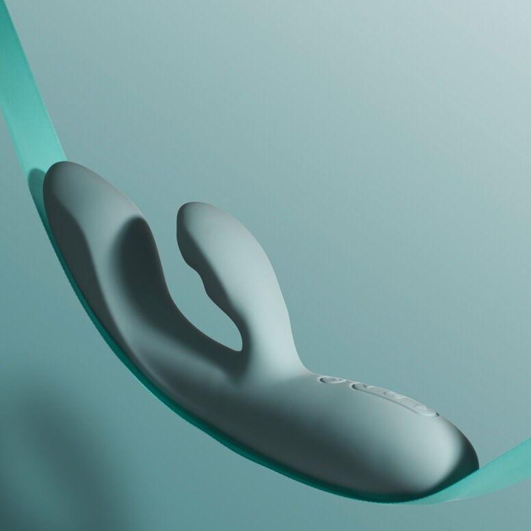 Grå SVAKOM Chika rabbitvibrator med varme, myk silikon og appstyring, vist på et turkis bånd.