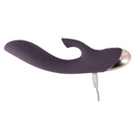 Mørk lilla silikon klitorissuger og G-punktvibrator med buet skaft og gullfarget tupp, koblet til ladekabel.