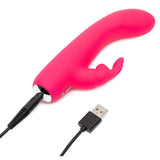 HappyRabbit Mini Rabbitvibrator i rosa silikon med buet tupp og kaninører, koblet til USB-ladekabel.