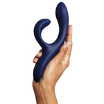 Hånd holder en dyp blå We-Vibe Nova 2 rabbitvibrator med fleksibel klitorisstimulator og ergonomisk design.