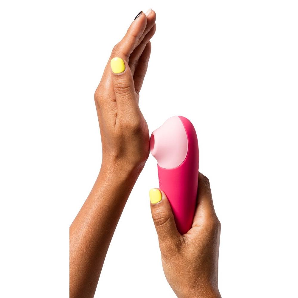 Mørke hender holder en kompakt, rosa Shine X ROMP lufttrykksvibrator med lyserosa tupp.