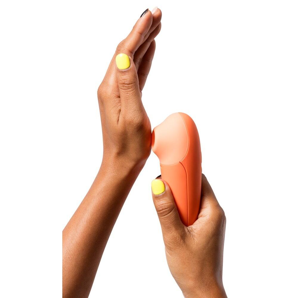 En kvinnes hender holder en kompakt, oransje ROMP Switch X sugevibrator med Pleasure Air Teknologi.