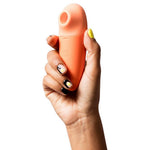 Hånd holder en kompakt, ferskenfarget ROMP Switch X sugevibrator med Pleasure Air Teknologi.