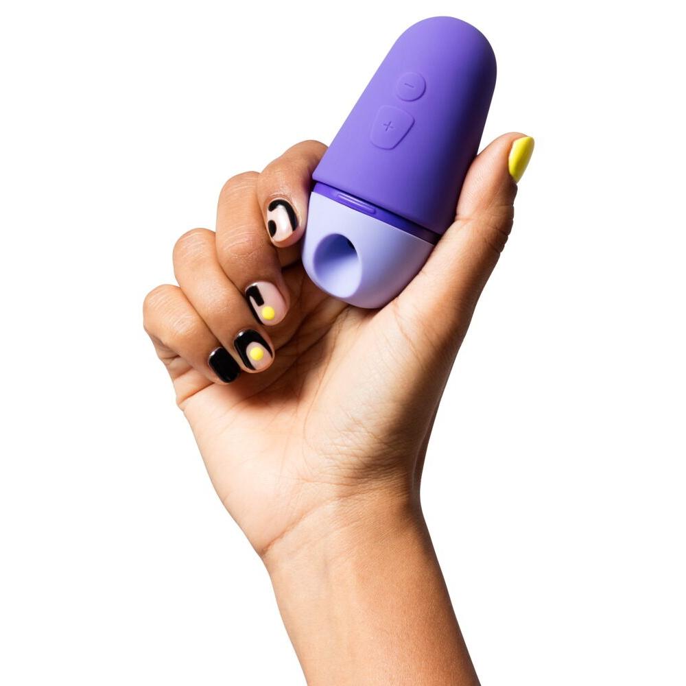 Hånd holder en kompakt, lilla ROMP Free X sugevibrator med myk silikon og kontrollknapper.
