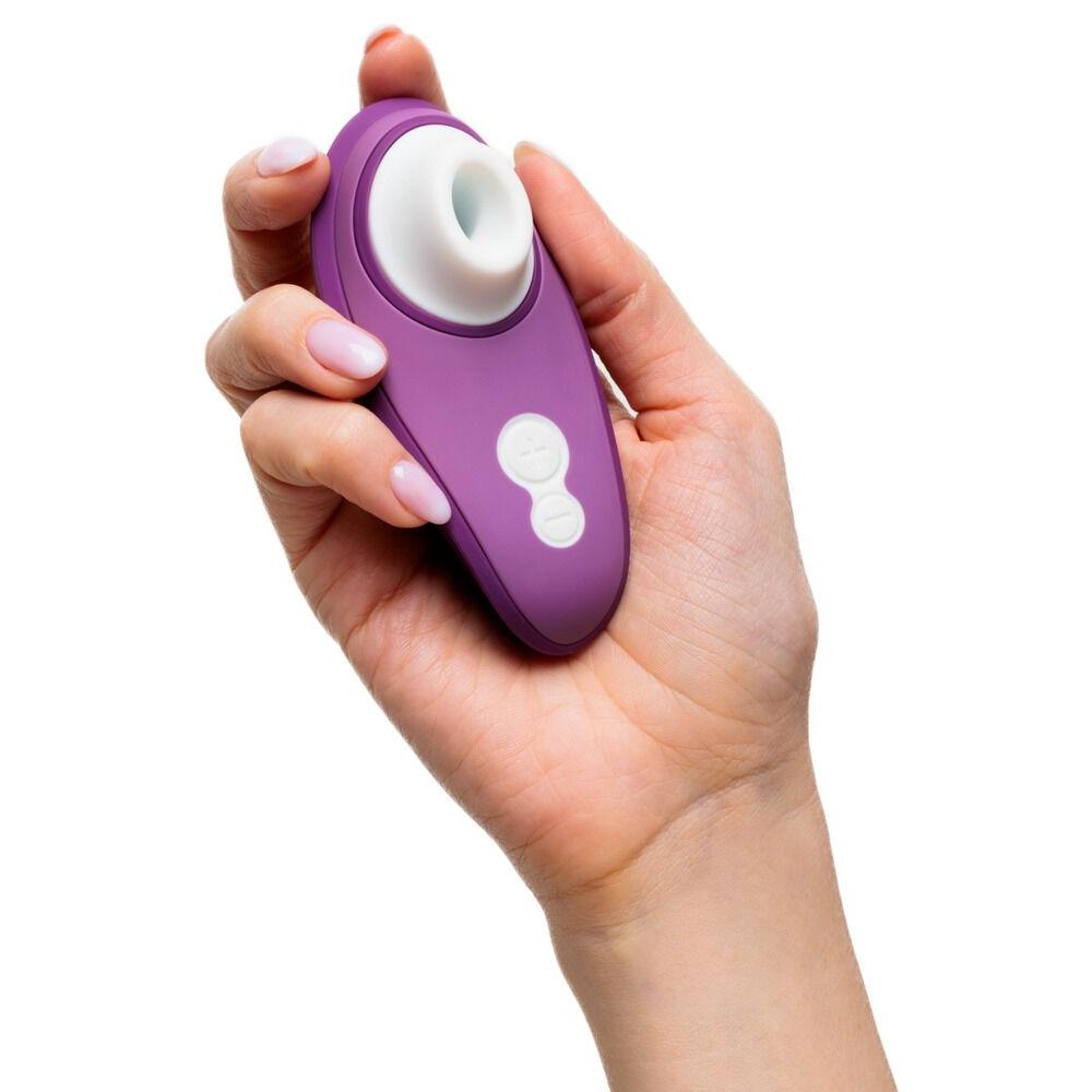 Hånd holder en lilla Womanizer Liberty 2 sugevibrator med hvit silikonmunnstykke og kontrollknapper.