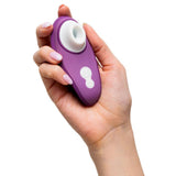 Hånd holder en lilla Womanizer Liberty 2 sugevibrator med hvit silikonmunnstykke og kontrollknapper.
