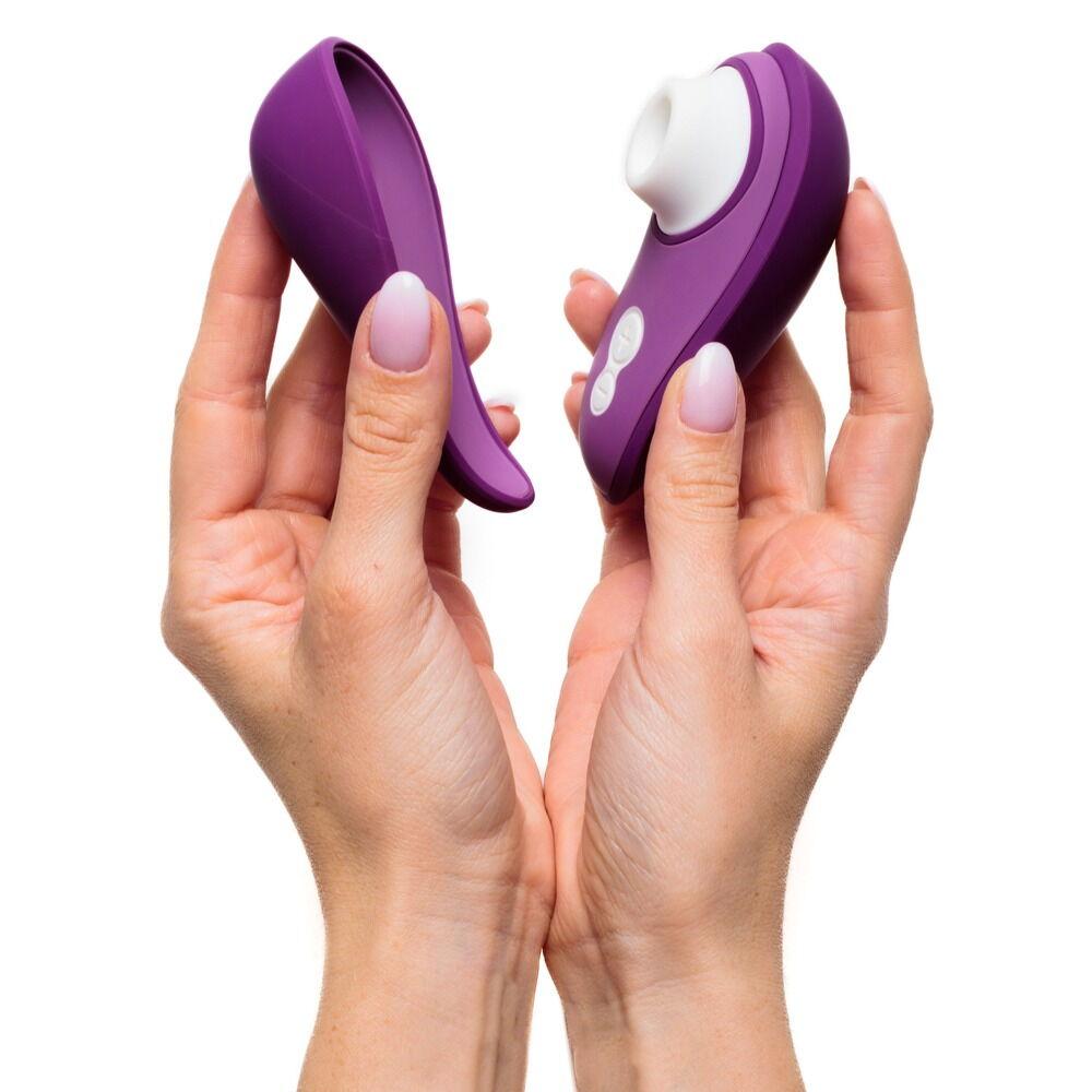 Hender holder en lilla Womanizer Liberty 2 sugevibrator med hvitt munnstykke og matchende magnetdeksel.