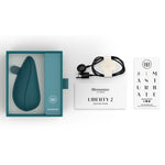 Mørkegrønn Womanizer Liberty 2 sugevibrator i åpen eske med ladekabel og manualer.