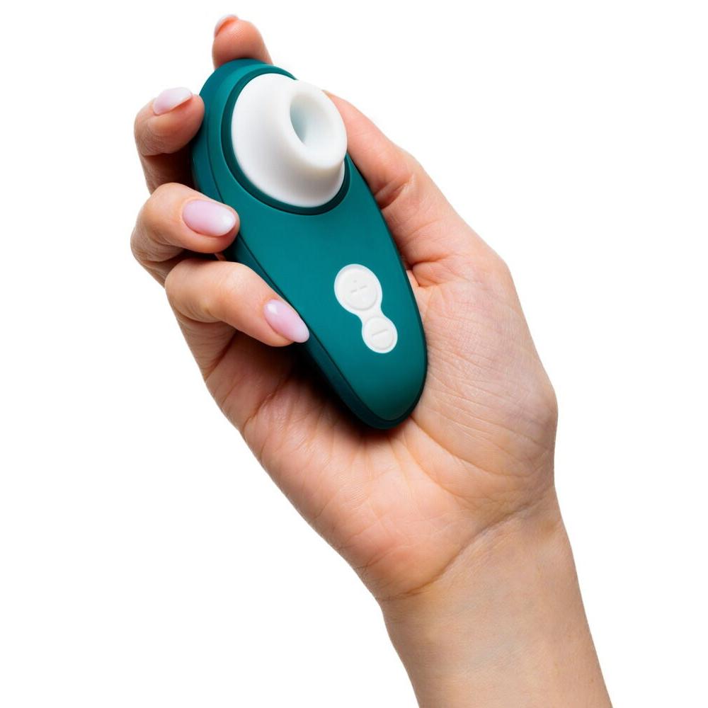 Hånd holder en mørkegrønn Womanizer Liberty 2 sugevibrator med hvit silikonmunnstykke og kontrollknapper.