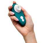 Hånd holder en mørkegrønn Womanizer Liberty 2 sugevibrator med hvit silikonmunnstykke og kontrollknapper.