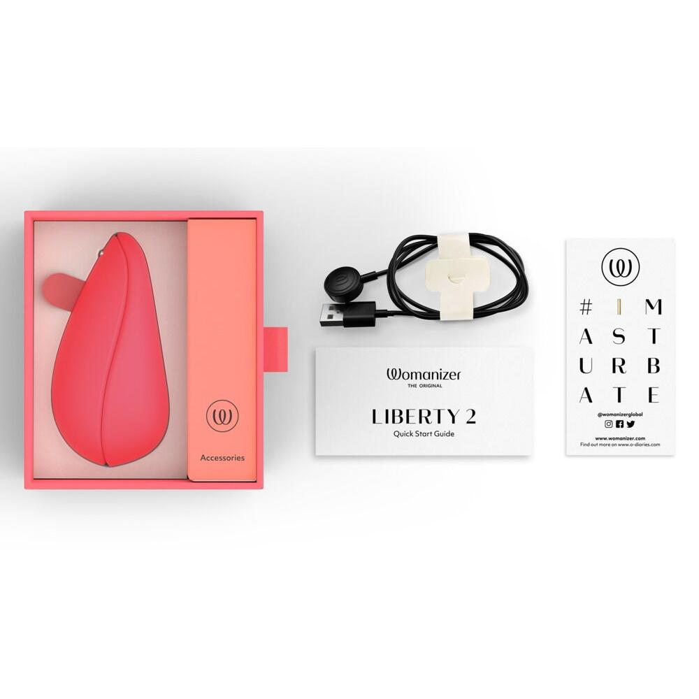 Womanizer Liberty 2 i korallrosa, med magnetdeksel, USB-ladekabel, og veiledninger.
