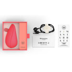 Womanizer Liberty 2 i korallrosa, med magnetdeksel, USB-ladekabel, og veiledninger.