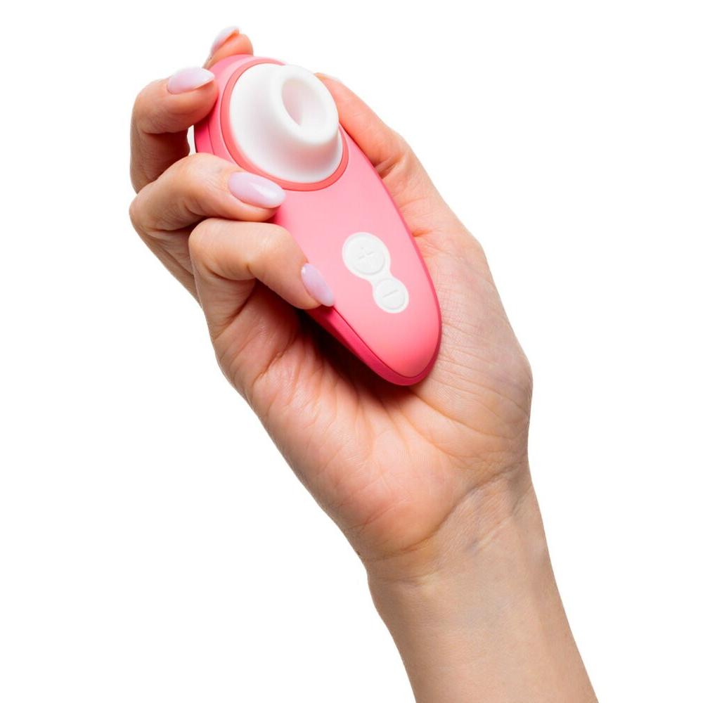 Hånd holder en korallrosa Womanizer Liberty 2 sugevibrator med hvitt stimuleringshode og kontrollknapper.