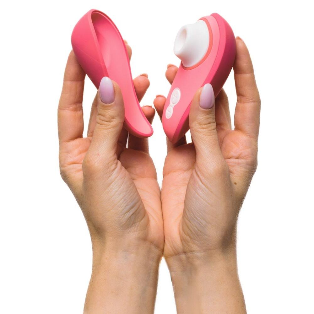 Hender holder en åpen Womanizer Liberty 2 i korallrosa med magnetdeksel og hvit stimulator.