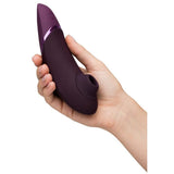 Hånd holder en Womanizer NEXT sugevibrator i elegant lilla med Soft Touch-overflate og metallisk aksent.