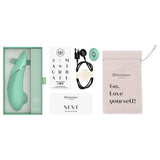 Mintgrønn Womanizer NEXT sugevibrator i åpen eske med lader, munnstykke, og oppbevaringspose.