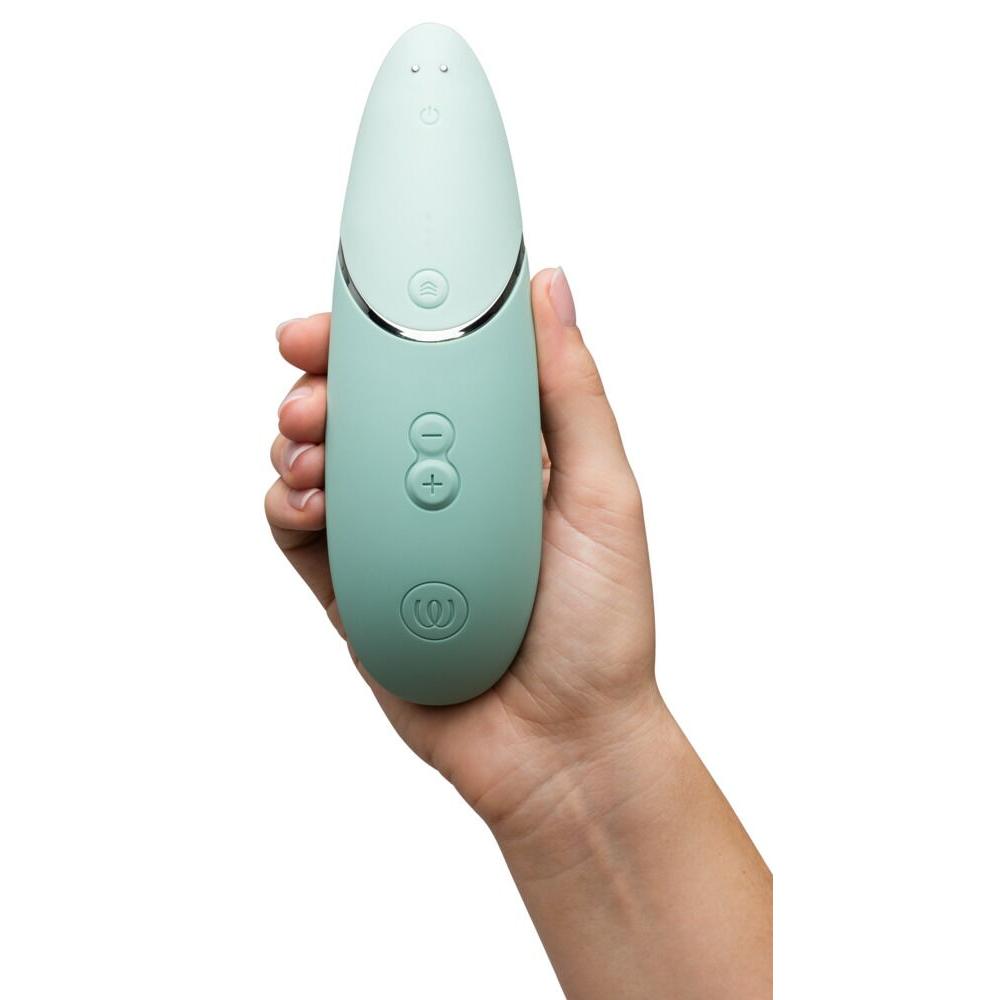 Hånd holder en Womanizer NEXT sugevibrator i mintgrønn med Soft Touch-overflate og sølvdetaljer.