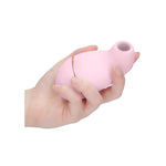 Hånd holder en lys rosa, silkemyk silikon sugevibrator med gullfarget detalj og åpen munnstykke.