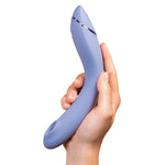 Hånd holder en lilla Womanizer OG G-punktvibrator med Pleasure Air-teknologi og elegant metallisk detalj.