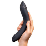 Hånd holder en Womanizer OG vibrator i matt sort silikon med sølvdetaljer, ergonomisk form.