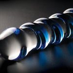 Klar glassdildo med blå spiralstruktur, skinnende på mørk bakgrunn.